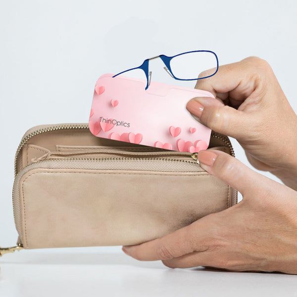 Blue ThinOptics Readers peeking out from a Pink Hearts Universal Pod being slipped into a clutch